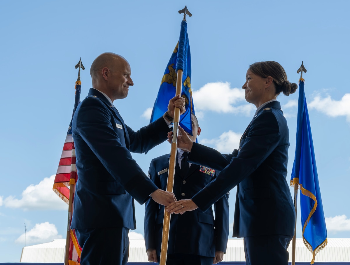 Brigadier general and a colonel hold a guidon on stage.