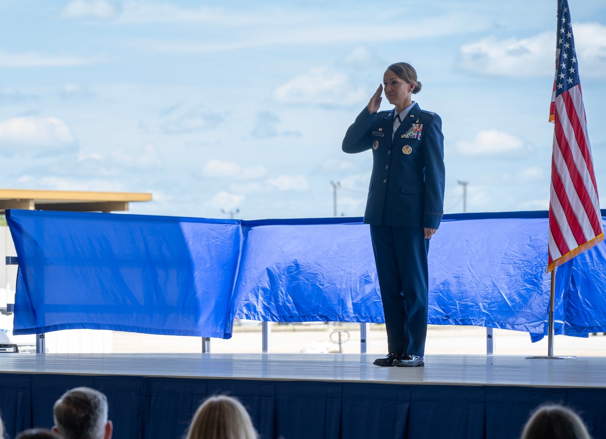 A female colonel stands on stage and salutes to the crowd.