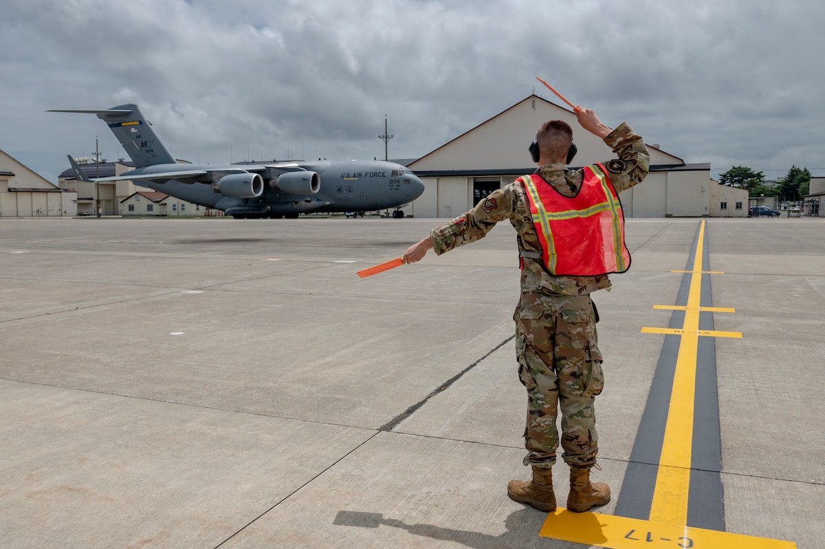 U.S. Air Force Airman 1st Class Kohl Rzepa, 35th Maintenance Squadron transient alert team member, marshals in a C-17 Globemaster III during exercise Resolute Force Pacific (REFORPAC) 2025 at Misawa Air Base, Japan, July 11, 2025. Mobility aircraft provide critical airlift, air refueling, aeromedical evacuation and command and control to project, connect, maneuver and sustain the Joint Force during the Department-Level Exercise Department of the Air Force series, including REFORPAC. (U.S. Air Force photo by Senior Airman Brittany Russell)