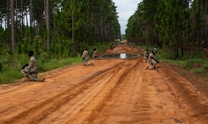 Airmen line up across the sides of a dirt, holding weapons and wearing tactical face masks.