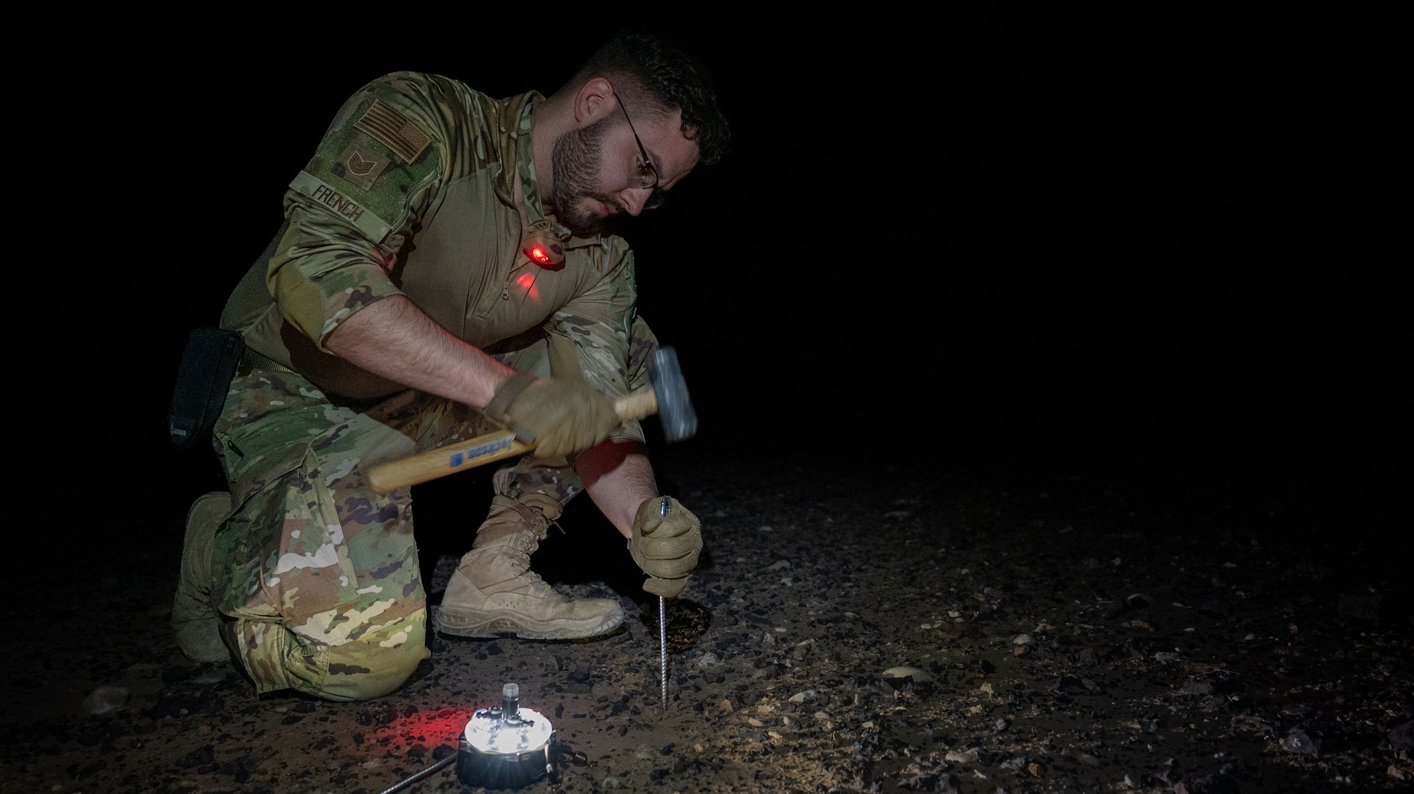 An Airman hammers a metal stake into the ground.