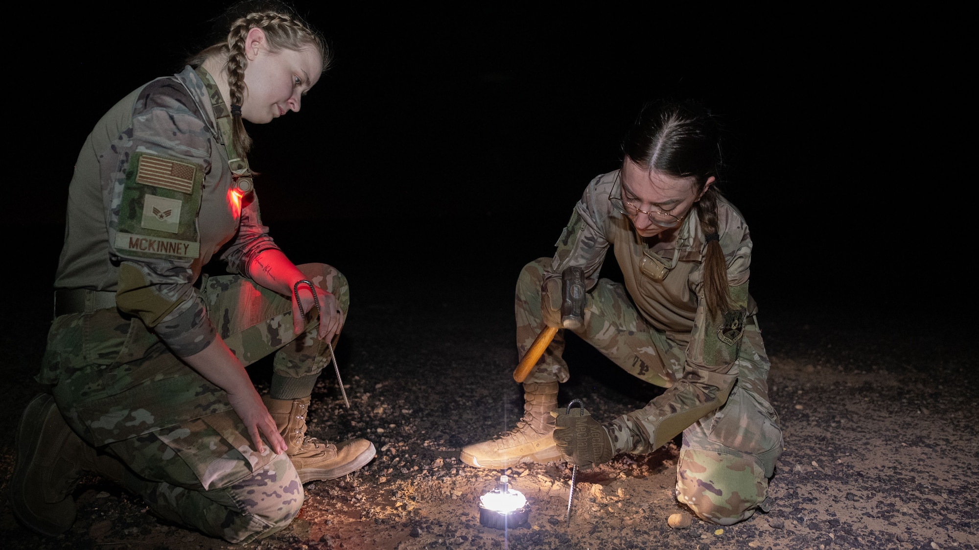 Two Airmen secure a metal stake in the ground.