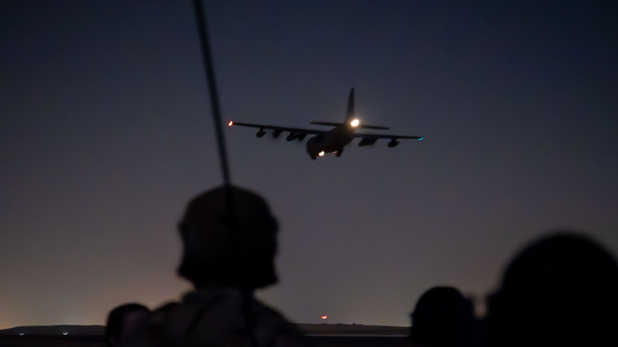 A silhouette of an Airman watching an HC-130J Combat King II fly overhead.