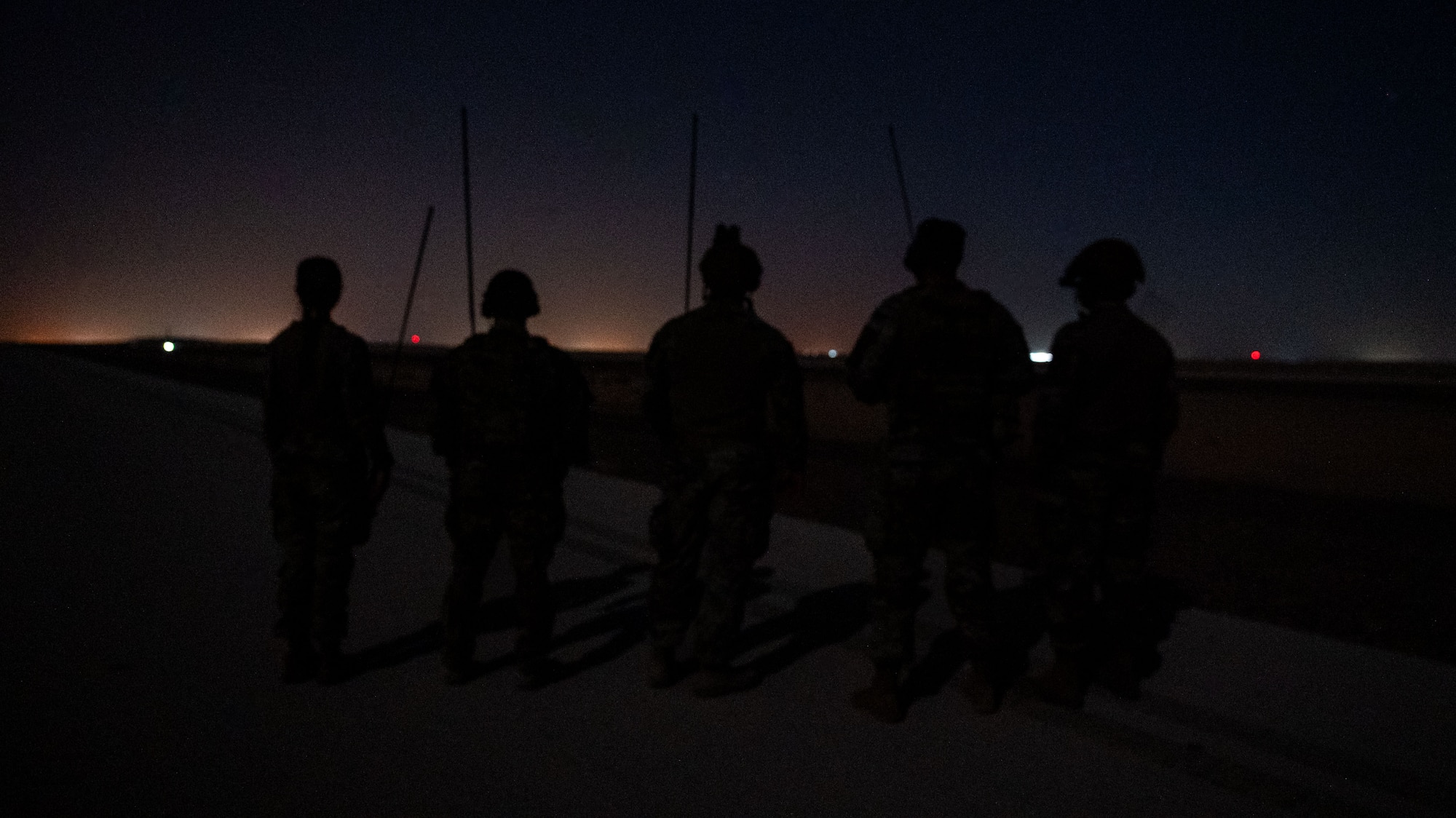 A silhouette photo of five Airmen monitoring an airfield.