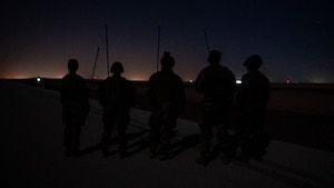 A silhouette photo of five Airmen monitoring an airfield.