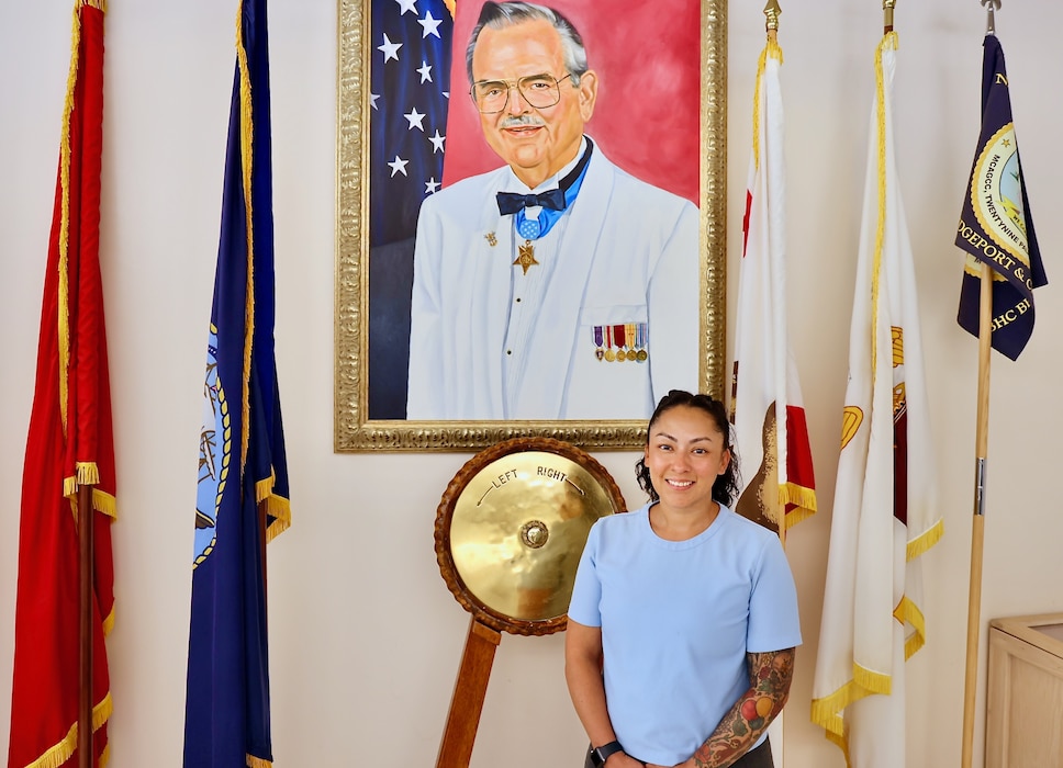 Jessica Hernandez, Physical Evaluation Board Liaison (PEBLO) at Navy Medicine Readiness and Training Command (NMRTC) Twentynine Palms, stands in front of a portrait of Medal of Honor recipient Robert E. Bush, the namesake of the hospital where she supports active-duty service members daily. In May, Hernandez was honored with the 2025 Department of the Navy Disability Evaluation System (DON DES) “All Star” Award for her exceptional contributions to medical readiness and disability case management. Her efforts led to a 50% improvement in data accuracy, streamlined medical evaluation board processing, and improved outcomes for more than 12,000 service members across three geographically dispersed units — all while serving as the sole PEBLO (U.S. Navy photo by Christopher C. Jones, NHTP/NMRTC Twentynine Palms public affairs officer).