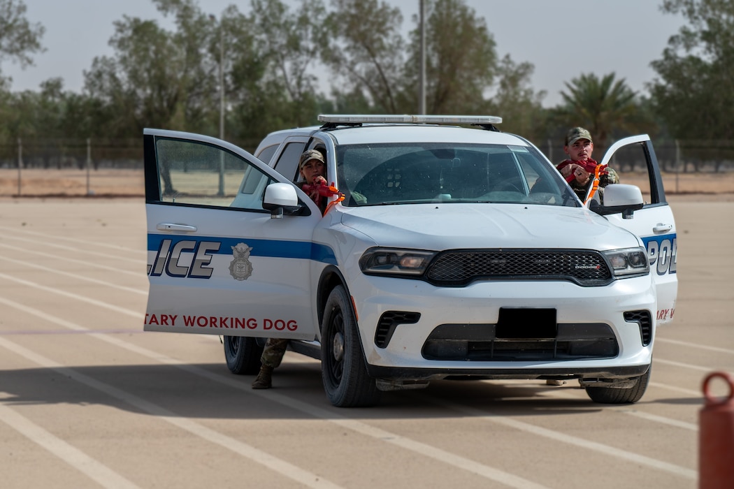 Two USAF Airmen with mock weapons stand behind a vehicle