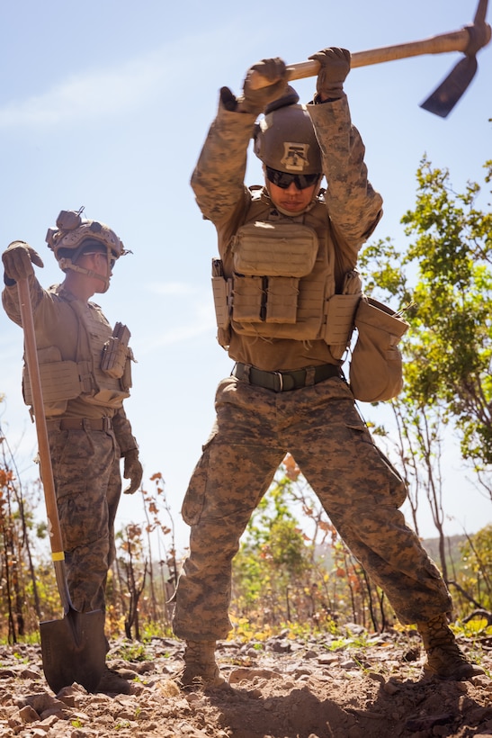 U.S. Marine Corps Cpl. Sutmai Karing, right, a field artillery cannoneer with Kilo Battery, 3rd Battalion, 11th Marine Regiment, Marine Rotational Force – Darwin 25.3, digs into the ground with a pickaxe during Talisman Sabre 25 in the  Northern Territory, Australia, July 11, 2025.