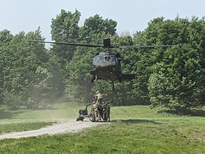 A UH-60M Black Hawk helicopter assigned to the New York National Guard's A Company, 3rd Battalion, 142nd Aviation, prepares to lift an M-117 howitzer belonging to the 1st Battalion, 258th Field Artillery during a training exercise at Fort Drum, New York on June 8, 2025.