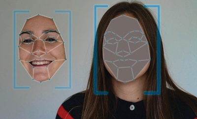 A woman is shown with facial recognition technology overlaying her face. On the left side of the image is a digital rendering of her smiling face with facial landmark points connected by lines, and on the right, the actual woman’s face is covered by a shaded facial map with similar landmarks. Blue rectangular frames highlight both the rendered and actual faces, indicating biometric analysis.