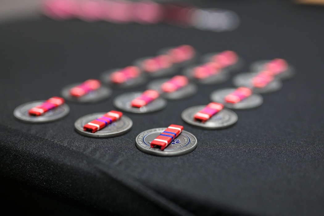 United States Air Force Noncommissioned Officer Professional Military Education Graduate ribbons sit on Airman Leadership coins during the Airman Leadership School Class 25-E Graduation Ceremony at the Powell Event Center, Goodfellow Air Force Base, Texas, July 10, 2025. ALS is a five-week course designed to prepare senior airmen to assume supervisory duties through instruction in leadership, followership and written and oral communication skills. (U.S. Air Force photo by Senior Airman Evelyn J. D’Errico)