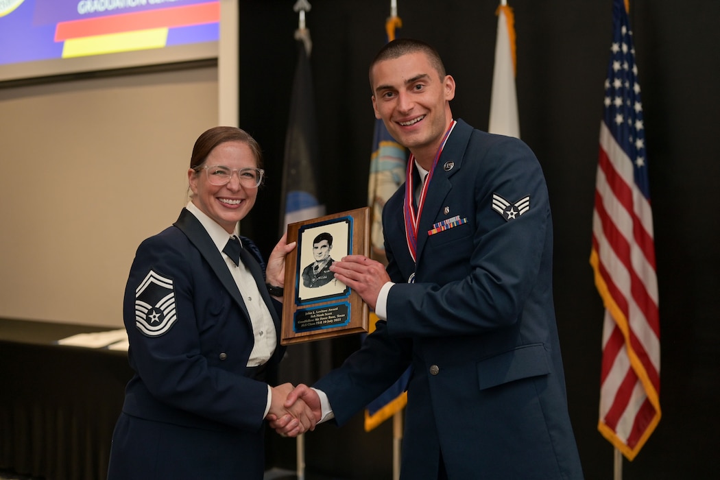 U.S. Air Force Senior Master Sgt. Jessica Dial, 17th Training Wing military training leader superintendent, presents Senior Airman Noah Scott, 17th Operational Medical Readiness Squadron ophthalmic technician, the John L. Levitow award during the ALS Class 25-E graduation at the Powell Event Center, Goodfellow Air Force Base, Texas, July 10, 2025. The John L. Levitow Award is the highest accolade in professional military education and is presented to the highest-performing graduate in each iteration of ALS. (U.S. Air Force photo by Senior Airman Evelyn J. D’Errico)