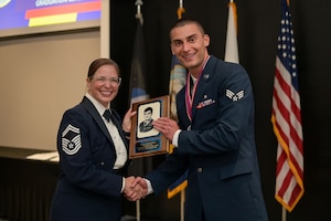 U.S. Air Force Senior Master Sgt. Jessica Dial, 17th Training Wing military training leader superintendent, presents Senior Airman Noah Scott, 17th Operational Medical Readiness Squadron ophthalmic technician, the John L. Levitow award during the ALS Class 25-E graduation at the Powell Event Center, Goodfellow Air Force Base, Texas, July 10, 2025. The John L. Levitow Award is the highest accolade in professional military education and is presented to the highest-performing graduate in each iteration of ALS. (U.S. Air Force photo by Senior Airman Evelyn J. D’Errico)