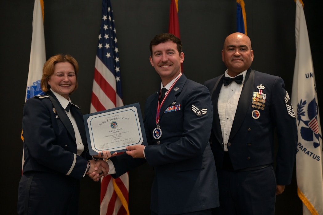 U.S. Air Force Col. Angelina Maguinness, 17th Training Wing commander, and Chief Master Sgt. Jason Ramon, 17th Mission Support Group senior enlisted leader, present Senior Airman Trey Watts, 17th TRW military justice paralegal, with the Airman Leadership School diploma during the ALS Class 25-E graduation at the Powell Event Center, Goodfellow Air Force Base, Texas, July 10, 2025. ALS is a five-week course designed to prepare senior airmen to assume supervisory duties through instruction in leadership, followership and written and oral communication skills. (U.S. Air Force photo by Senior Airman Evelyn J. D’Errico)