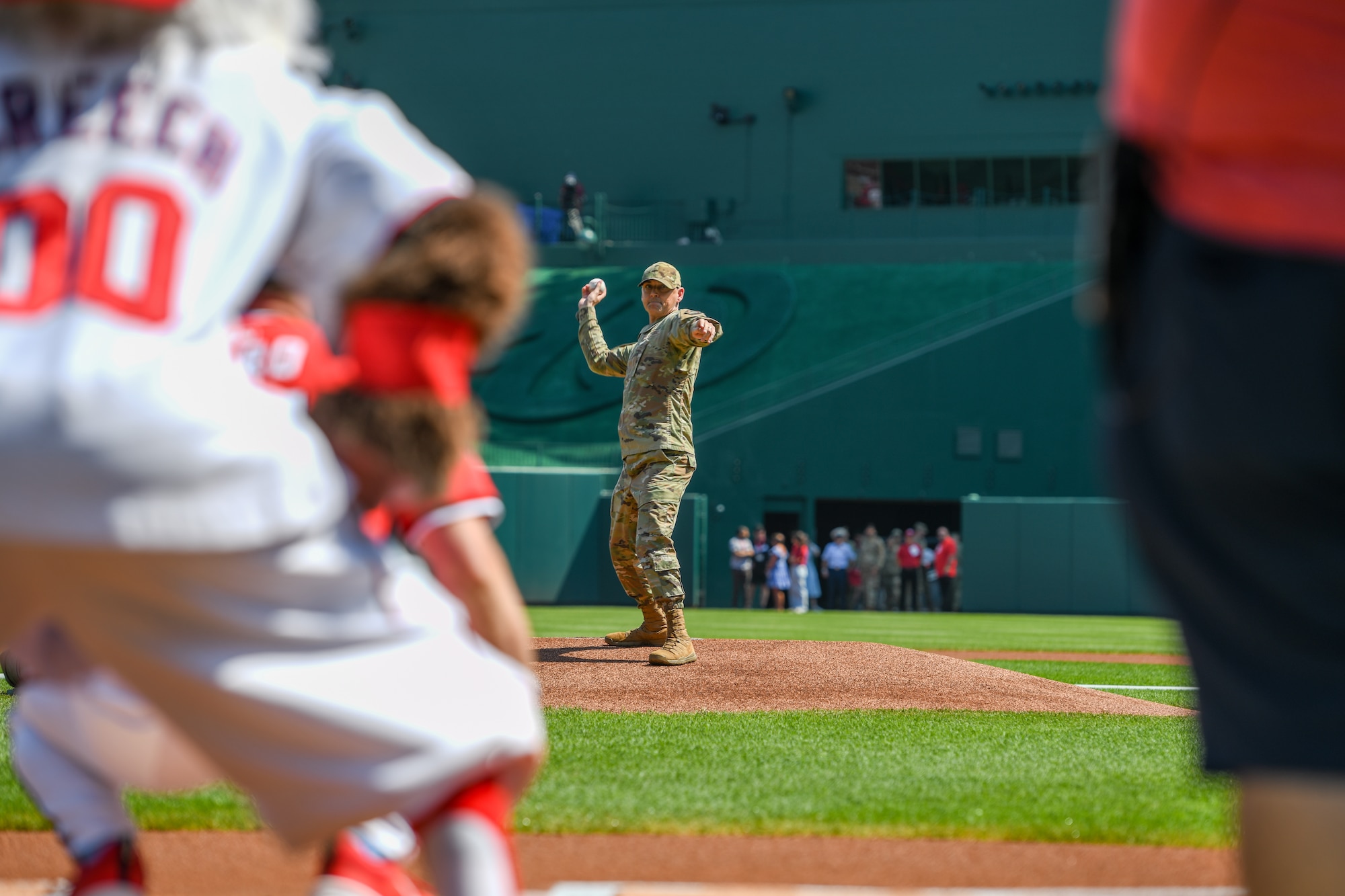 A service members pitches a ball on a baseball field.