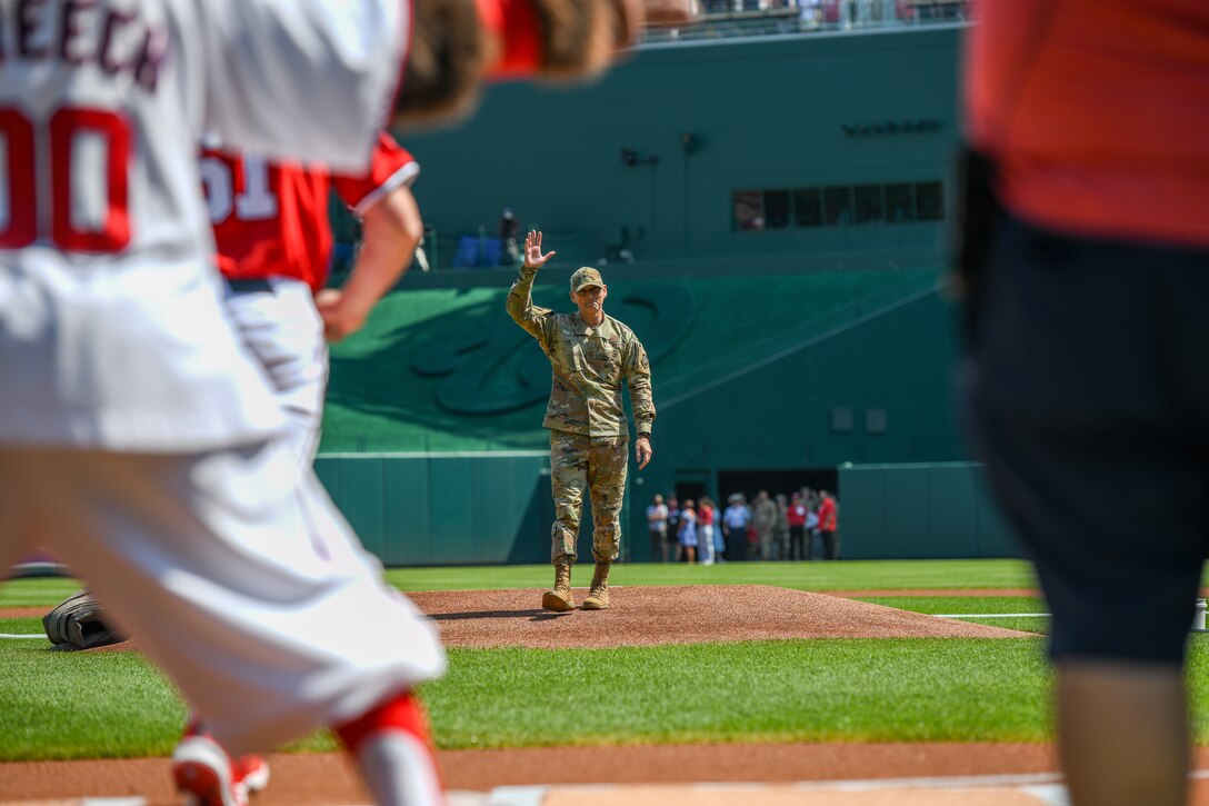 A service member waves form the pitcher's mound of a baseball field.