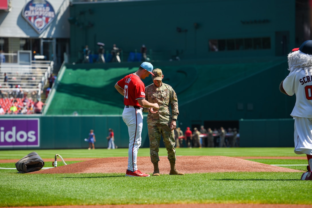 A baseball player hands a service member a ball on a baseball field.