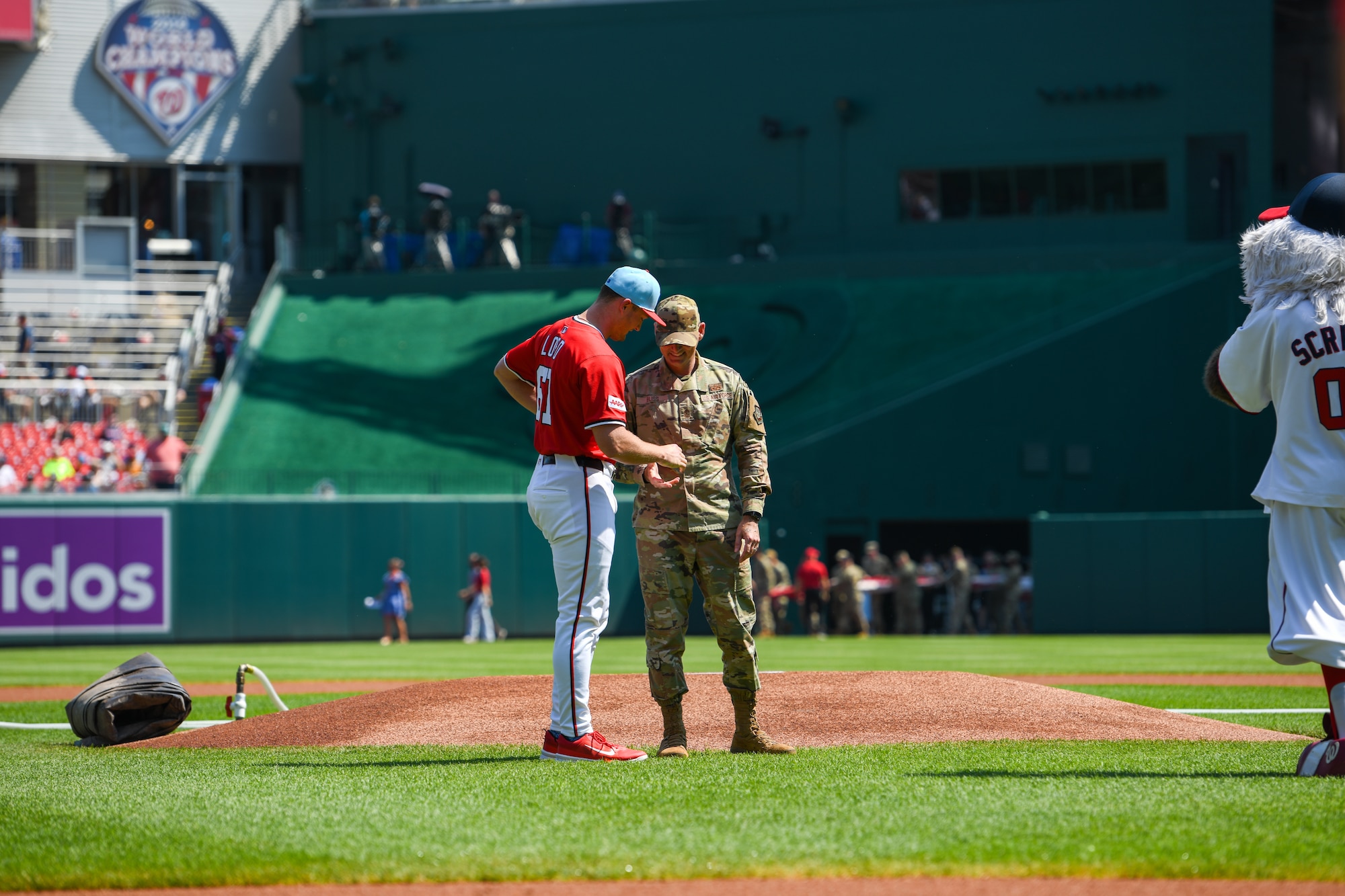 A baseball player hands a service member a ball on a baseball field.