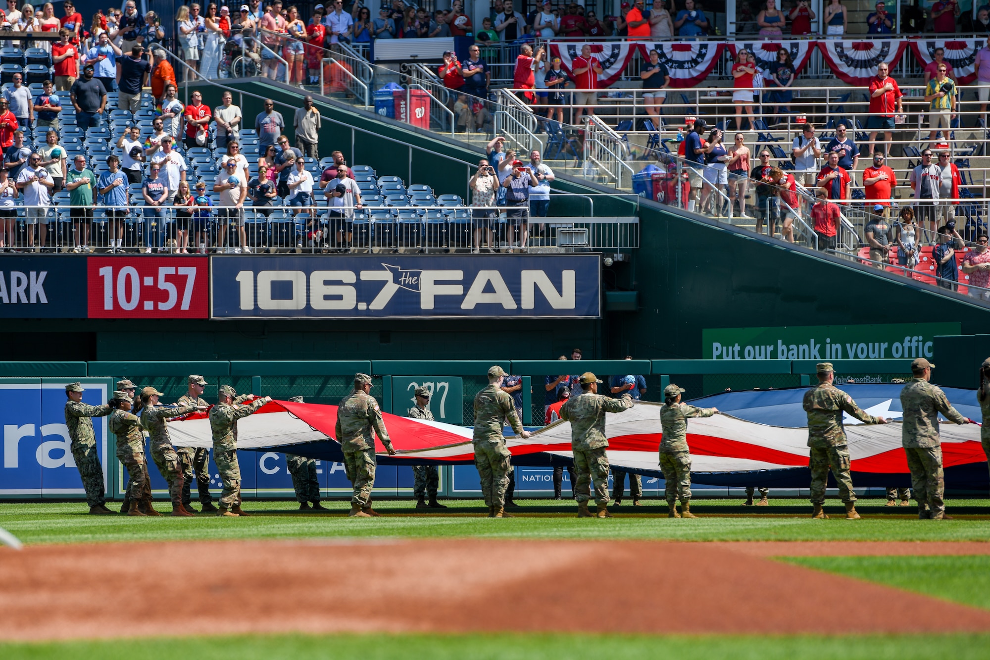 Service members wave an American Flag on a baseball field.