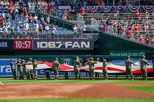Service members wave an American Flag on a baseball field.