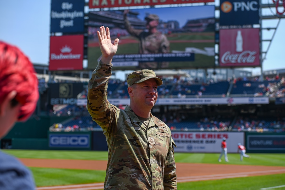 Service member waves from a baseball field.