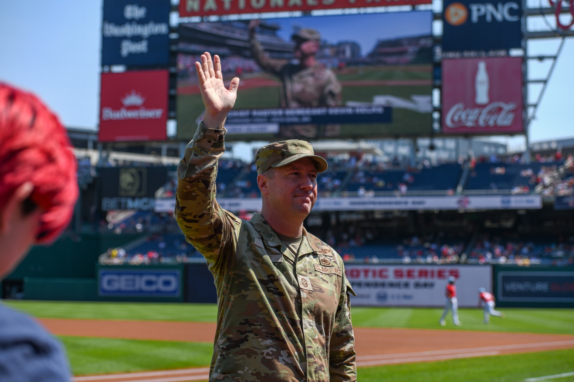 Service member waves from a baseball field.