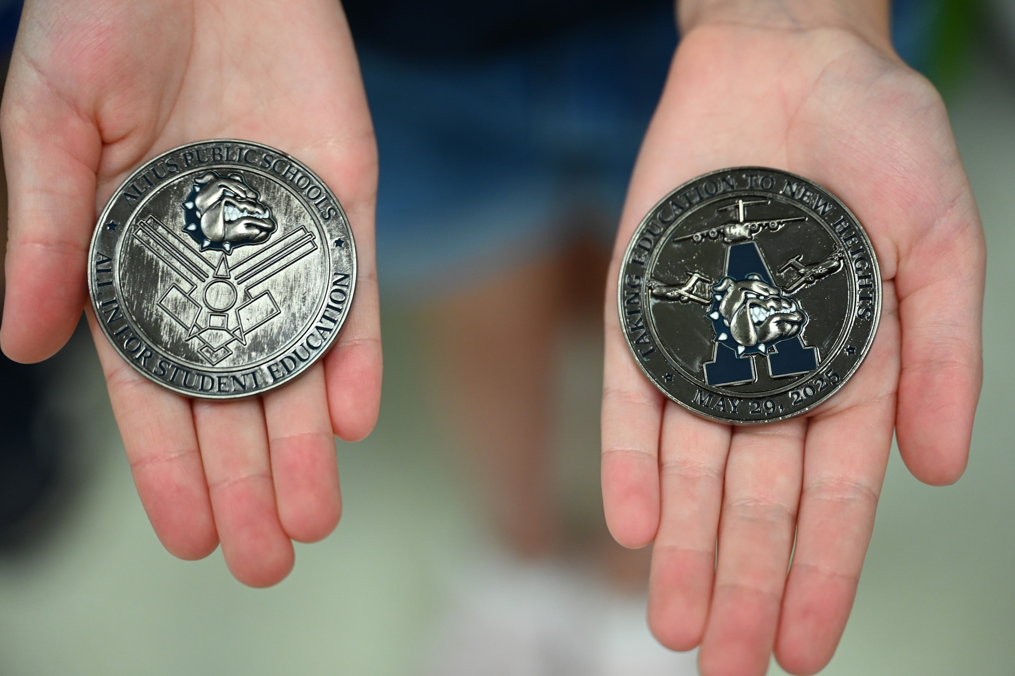Two L. Mendel Rivers Elementary School coins are held by a student at a ground breaking ceremony at Altus Air Force Base, Oklahoma, July 8, 2025. The ceremony was held to celebrate the beginning of construction for a brand new schoolhouse. (U.S. Air Force photo by Airman 1st Class Nathan Langston)