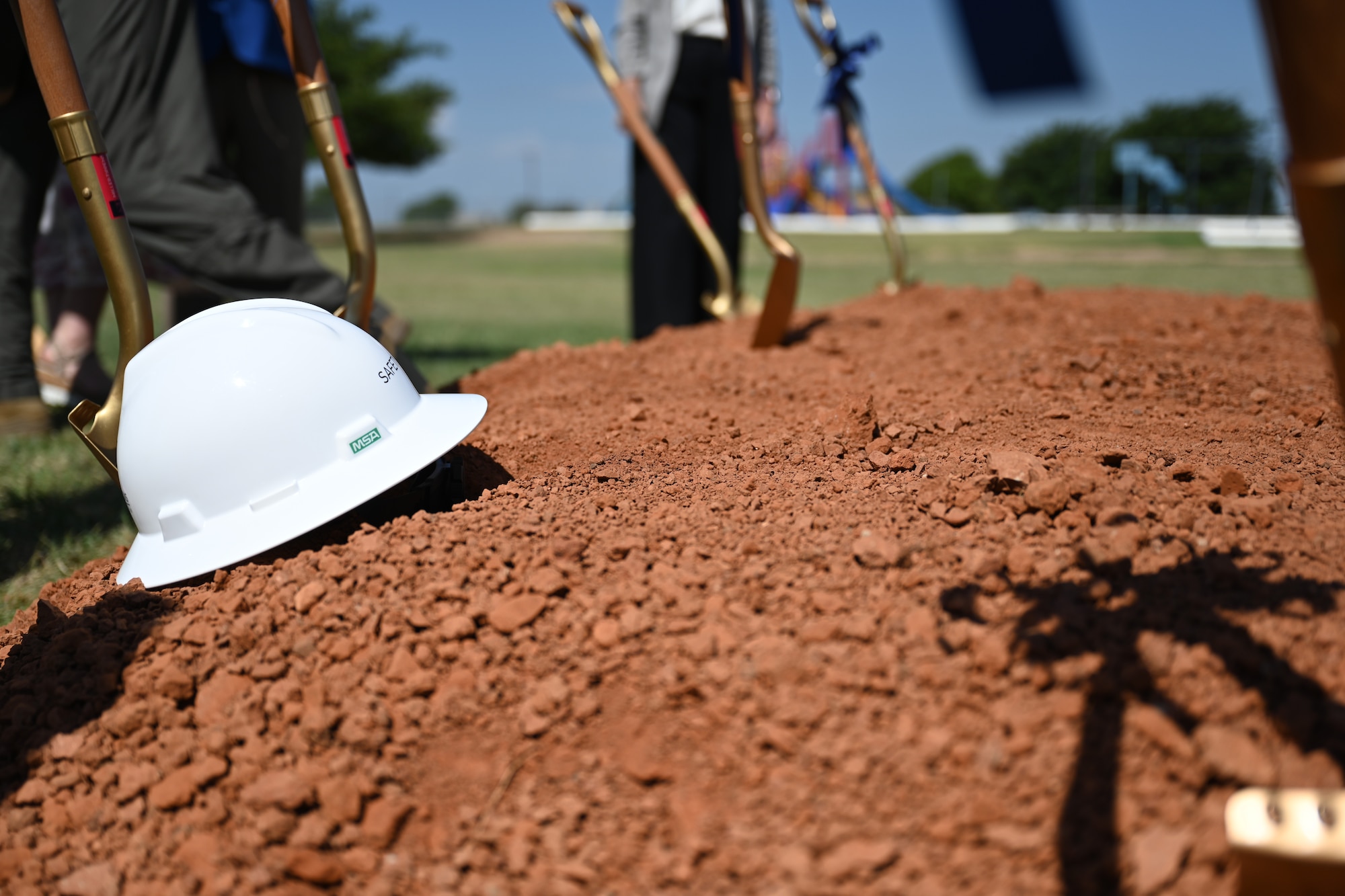 Shovels and helmets are displayed at the site of the new elementary school at Altus Air Force Base, Oklahoma, July 8, 2025. The golden shovels were given out to 97th Air Mobility Wing leadership and distinguished guests to commemorate the ‘first dig’. (U.S. Air Force photo by Airman 1st Class Nathan Langston)