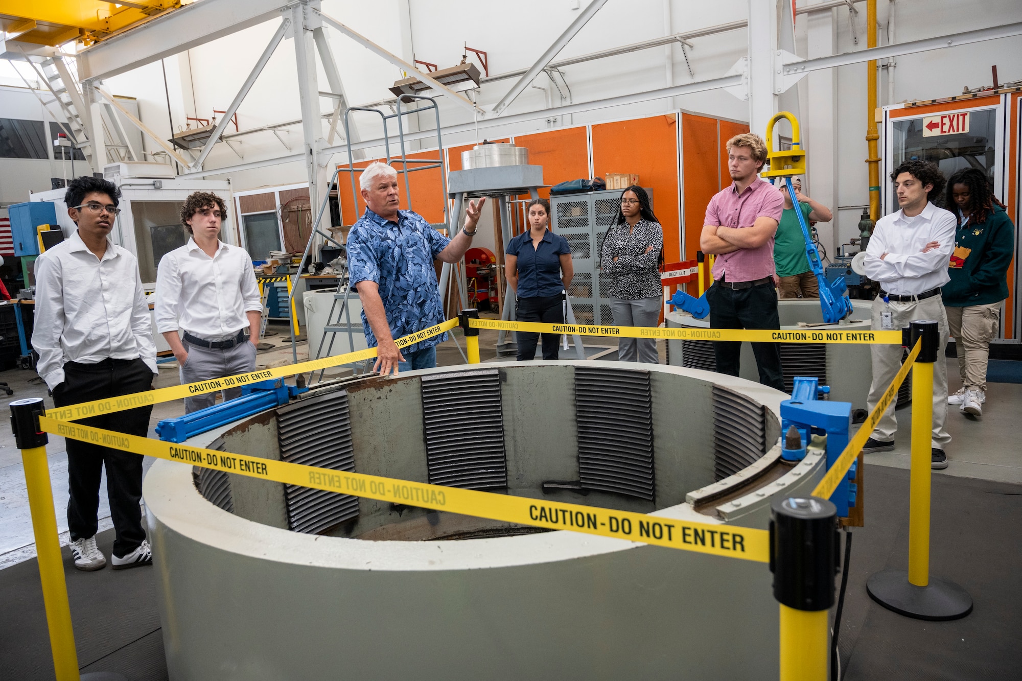 Man in a laboratory setting points into circular tank with interns on both sides of him