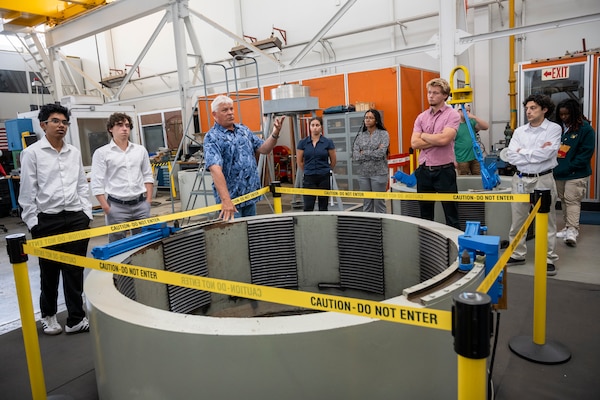 Man in a laboratory setting points into circular tank with interns on both sides of him
