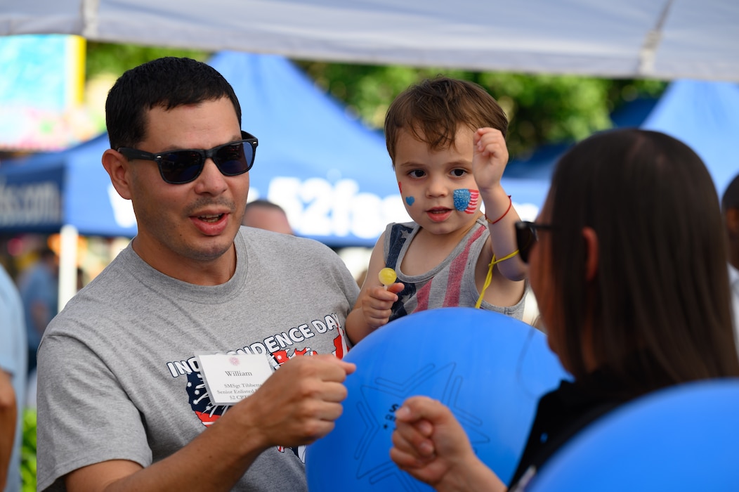 A man holds a child and fist bumps a woman.