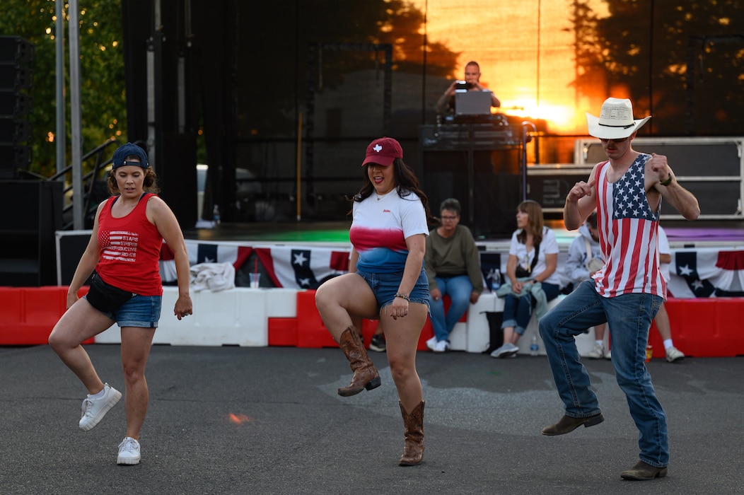 Three people line dance in front a stage.