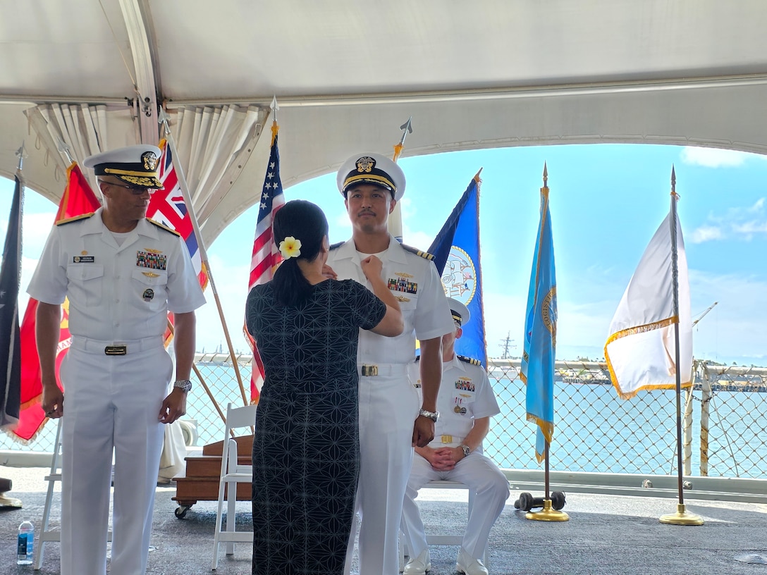 Wife pins insignia on her spouse's uniform during change of command ceremony.
