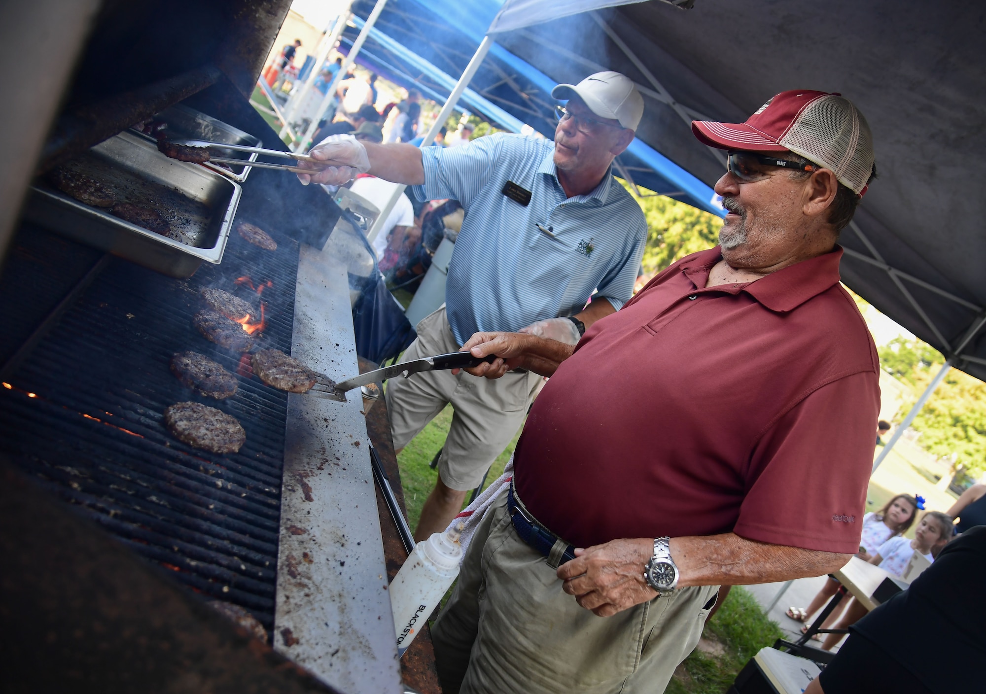 Two men flip burgers on a grill