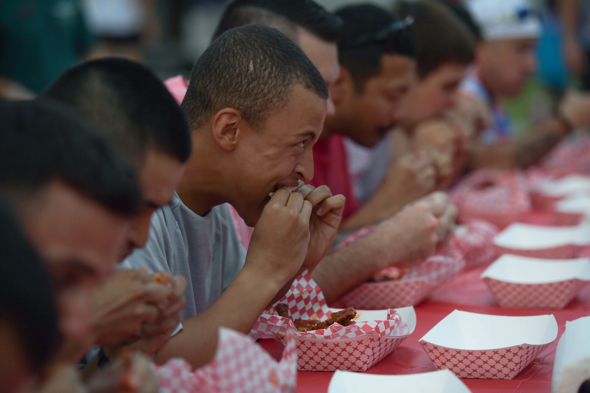 A group of men sit at a table eating hot wings in front of a crowd