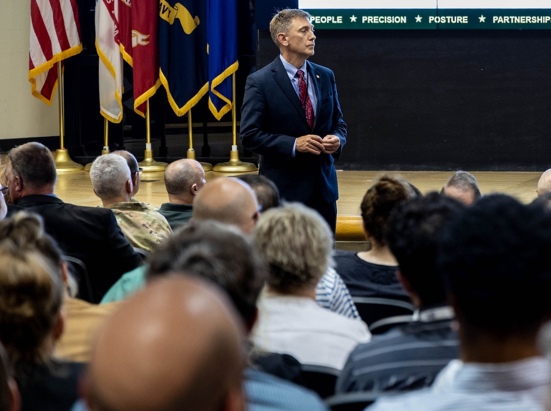 A man in a dark suit stands in a full auditorium as he listens to a question from the audience.