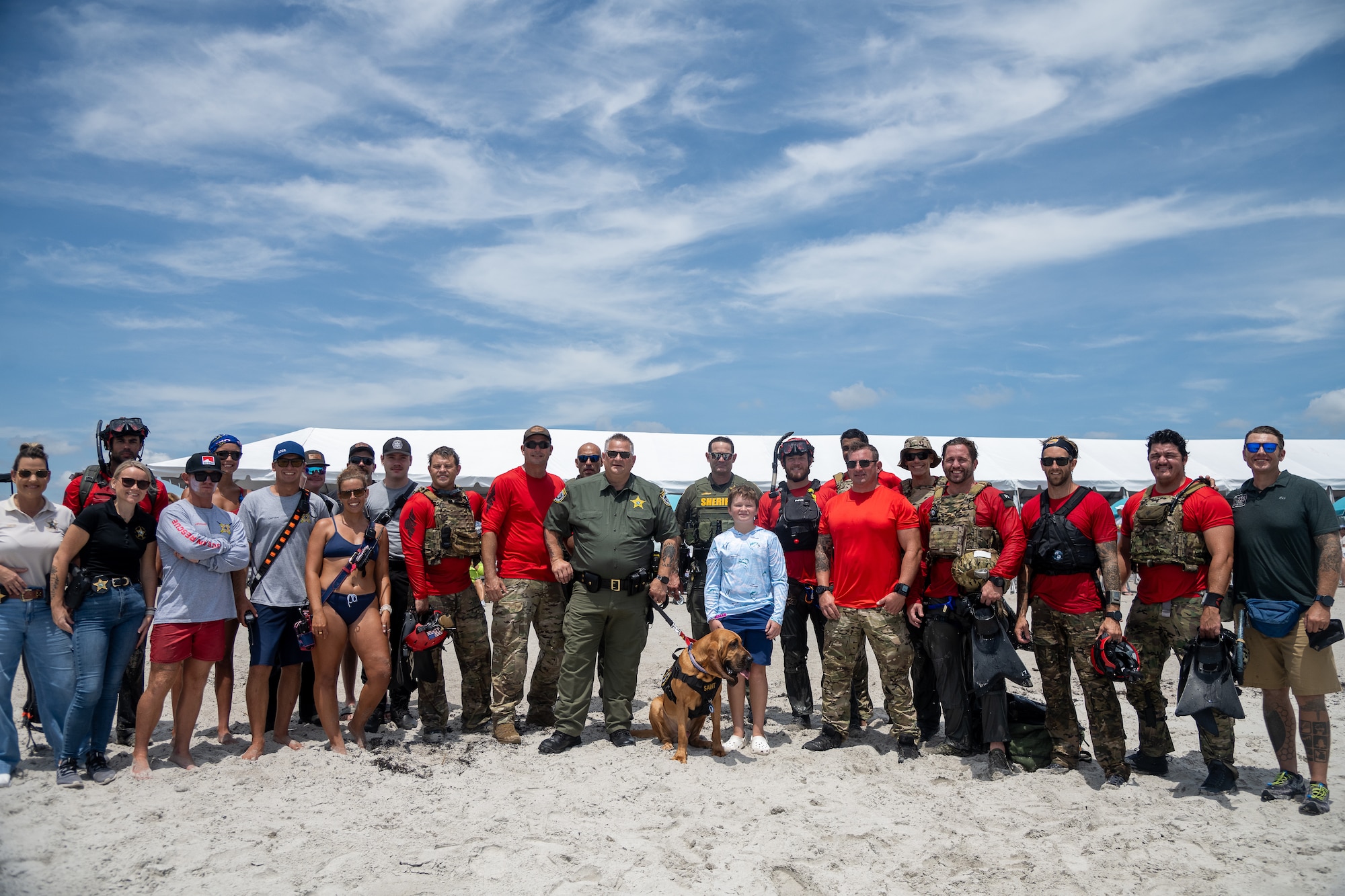 Jackson Posch, center, stands with members of the 920th Rescue Wing and Brevard County Sheriff’s Office deputies, including Sheriff Wayne Ivey and Saint Francis, the department’s bloodhound mascot trained to help locate missing children and adults, during the Cocoa Beach Air Show, July 12, 2025. The 920th Rescue Wing continues to honor Jackson’s father, Master Sgt. William Posch, a pararescueman who was killed in the 2018 crash of Jolly 51, by including Jackson in events and mentoring him as one of their own.