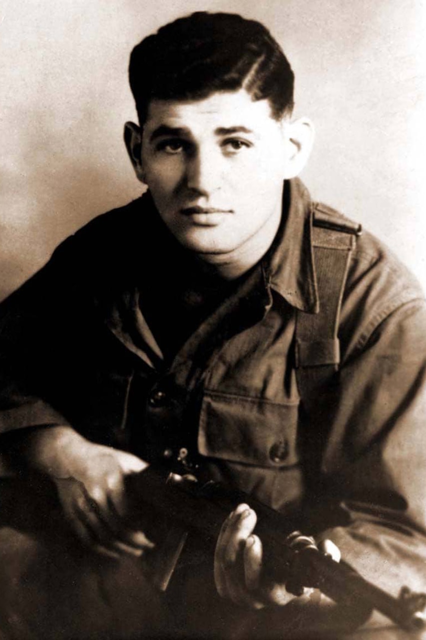 A man dressed in a military uniform poses for a photo while holding a weapon.