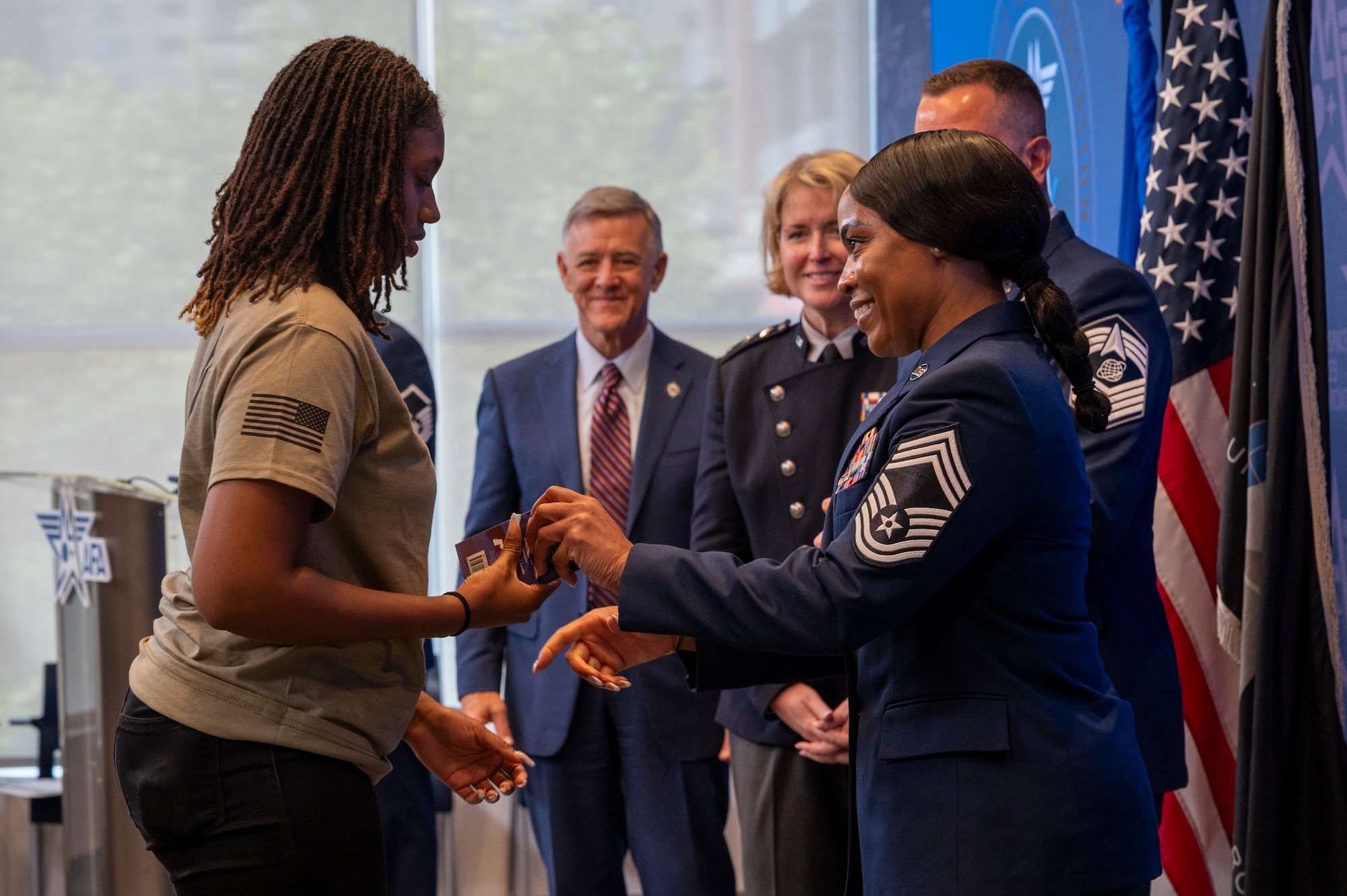 U.S. Air Force Chief Master Sgt. Ladiwina Gilly, the Senior Enlisted Leader of the 317th Recruiting Squadron, gives a copy of the U.S. Constitution and a challenge coin to a delayed entry program recruit during an enlistment ceremony at the Air & Space Forces Association headquarters in Arlington, Va., July 11, 2025. The efforts of the 317th RCS led to the recruitment of future Airmen and Guardians at the ceremony. (U.S. Air Force photo by Hayden Hallman)