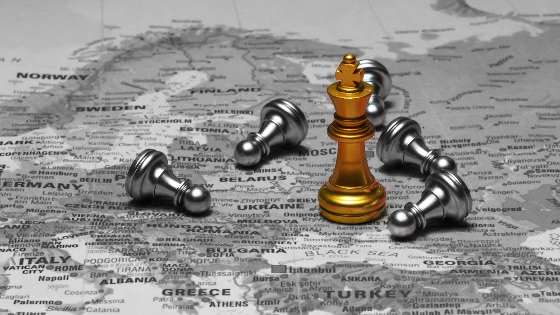 A black-and-white map of Europe and parts of Russia is overlaid with chess pieces. A prominent gold king stands in the area near Moscow, surrounded by toppled silver pawns, suggesting a geopolitical metaphor for dominance or conflict in the region.