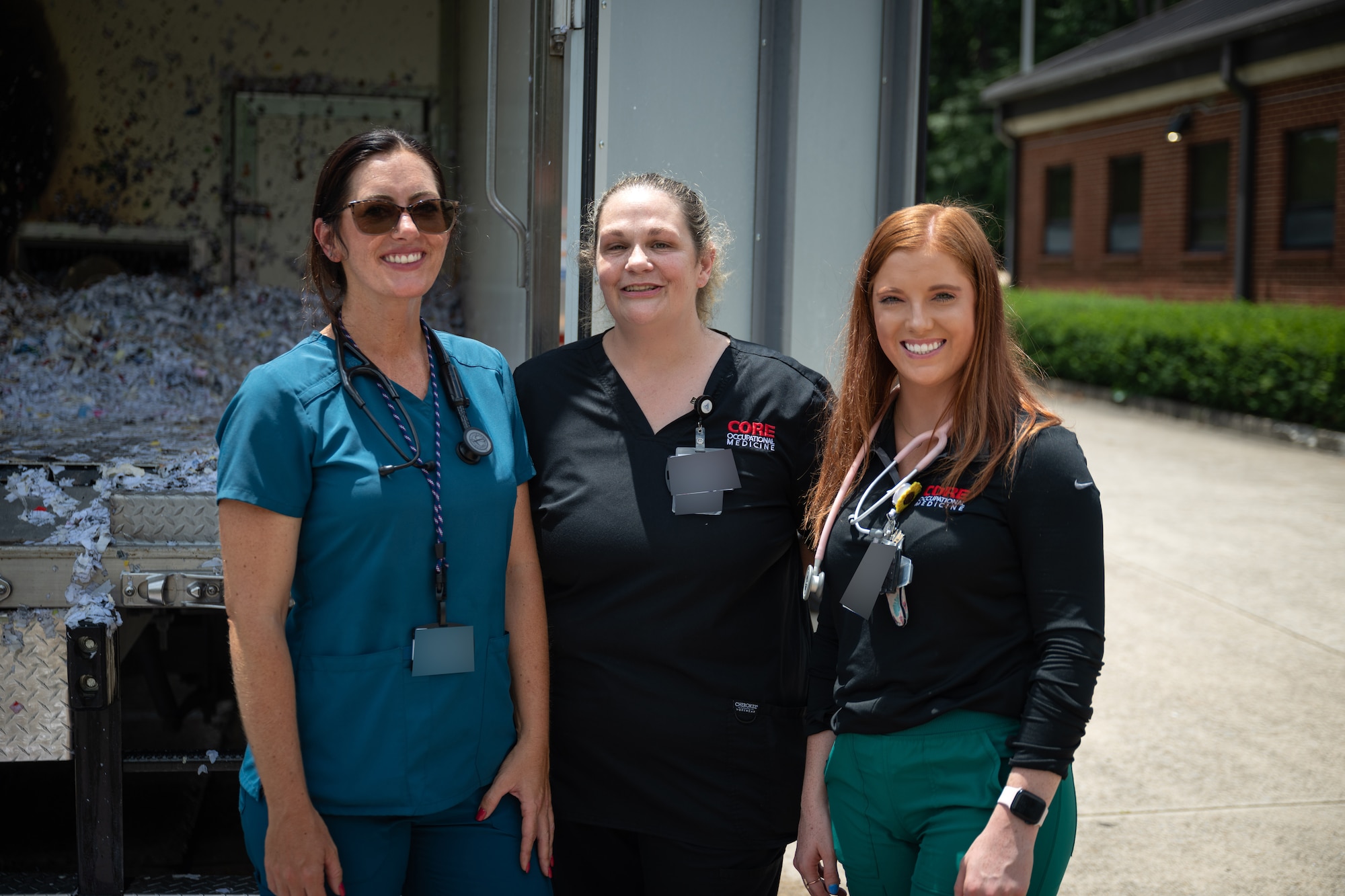 Amanda Van Pelt, Suzanne Hale and Kelsey Rob, pictured from left, pose for a photo after extinguishing a fire outside the Medical Aid Station at Arnold Air Force Base, Tenn., July 11, 2025. The three are staff members with CORE Occupational Medicine, a company subcontracted by the Arnold Engineering Development Complex Test Operations and Sustainment Contractor to provide basic medical services to TOS employees at Arnold AFB, headquarters of AEDC. The CORE team sprang into action when a truck collecting shredded materials unexpectedly caught fire. They used extinguishers to quickly put out the flames, preventing the fire from spreading and minimizing damage. (U.S. Air Force photo by Keith Thornburgh) (This image was altered by obscuring badges for security purposes)
