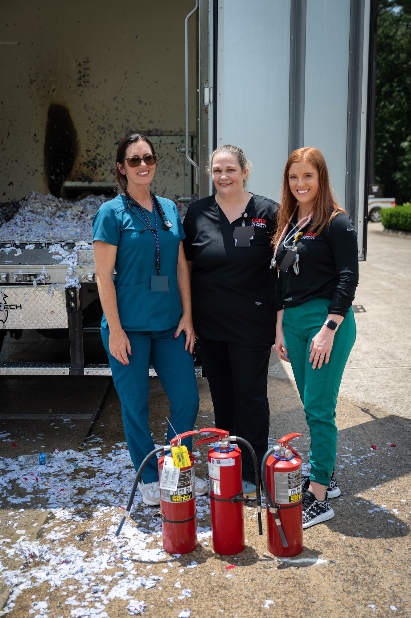 Amanda Van Pelt, Suzanne Hale and Kelsey Rob, pictured from left, pose for a photo after extinguishing a fire outside the Medical Aid Station at Arnold Air Force Base, Tenn., July 11, 2025. The three are staff members with CORE Occupational Medicine, a company subcontracted by the Arnold Engineering Development Complex Test Operations and Sustainment Contractor to provide basic medical services to TOS employees at Arnold AFB, headquarters of AEDC. The CORE team sprang into action when a truck collecting shredded materials unexpectedly caught fire. They used extinguishers to quickly put out the flames, preventing the fire from spreading and minimizing damage. (U.S. Air Force photo by Keith Thornburgh) (This image was altered by obscuring badges for security purposes)