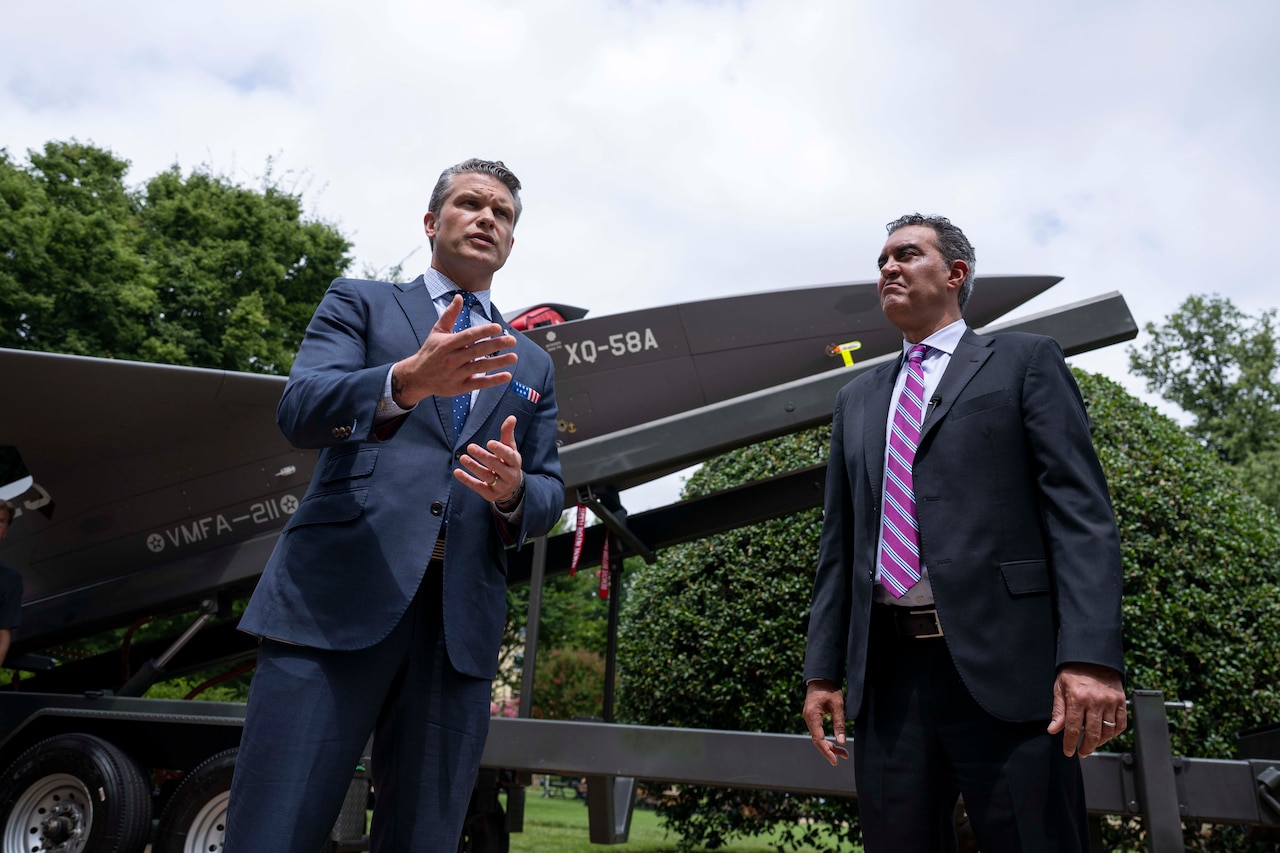 Two men stand in front of a drone on display.