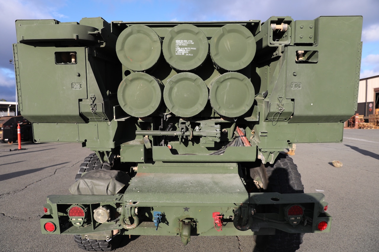 The back side of a combat vehicle is painted in Army green and features the bottoms of six round rocket launch tubes.