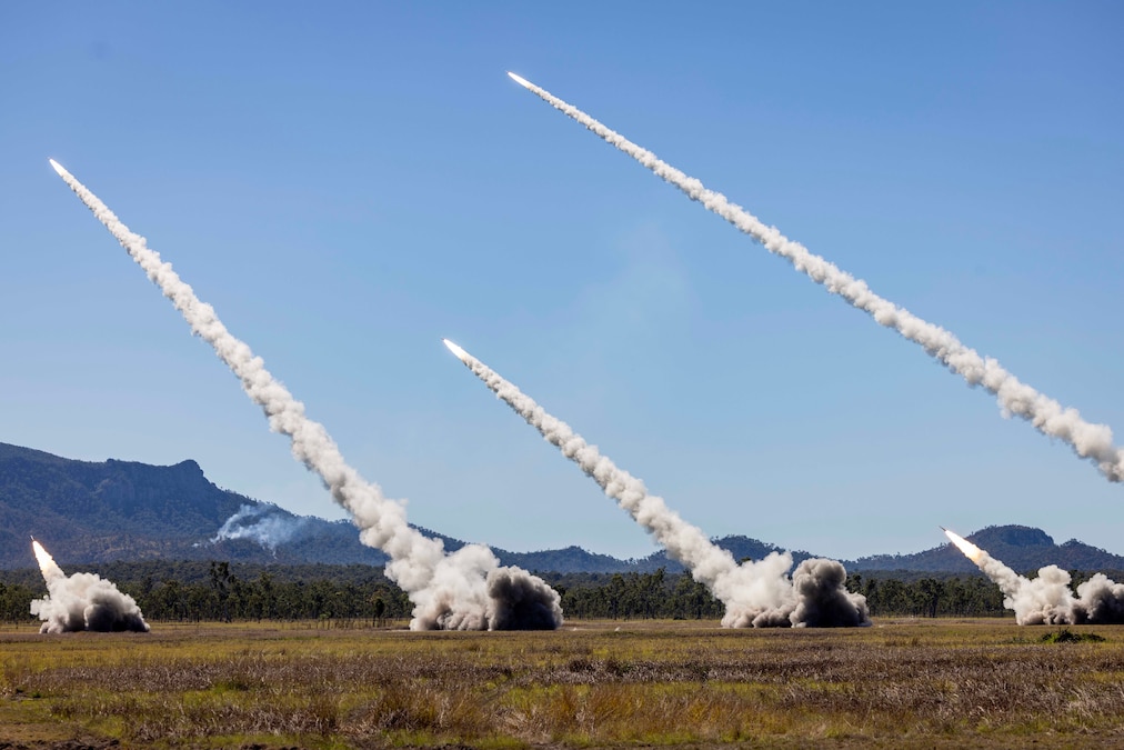 Fire rockets are fired from a field under blue skies.