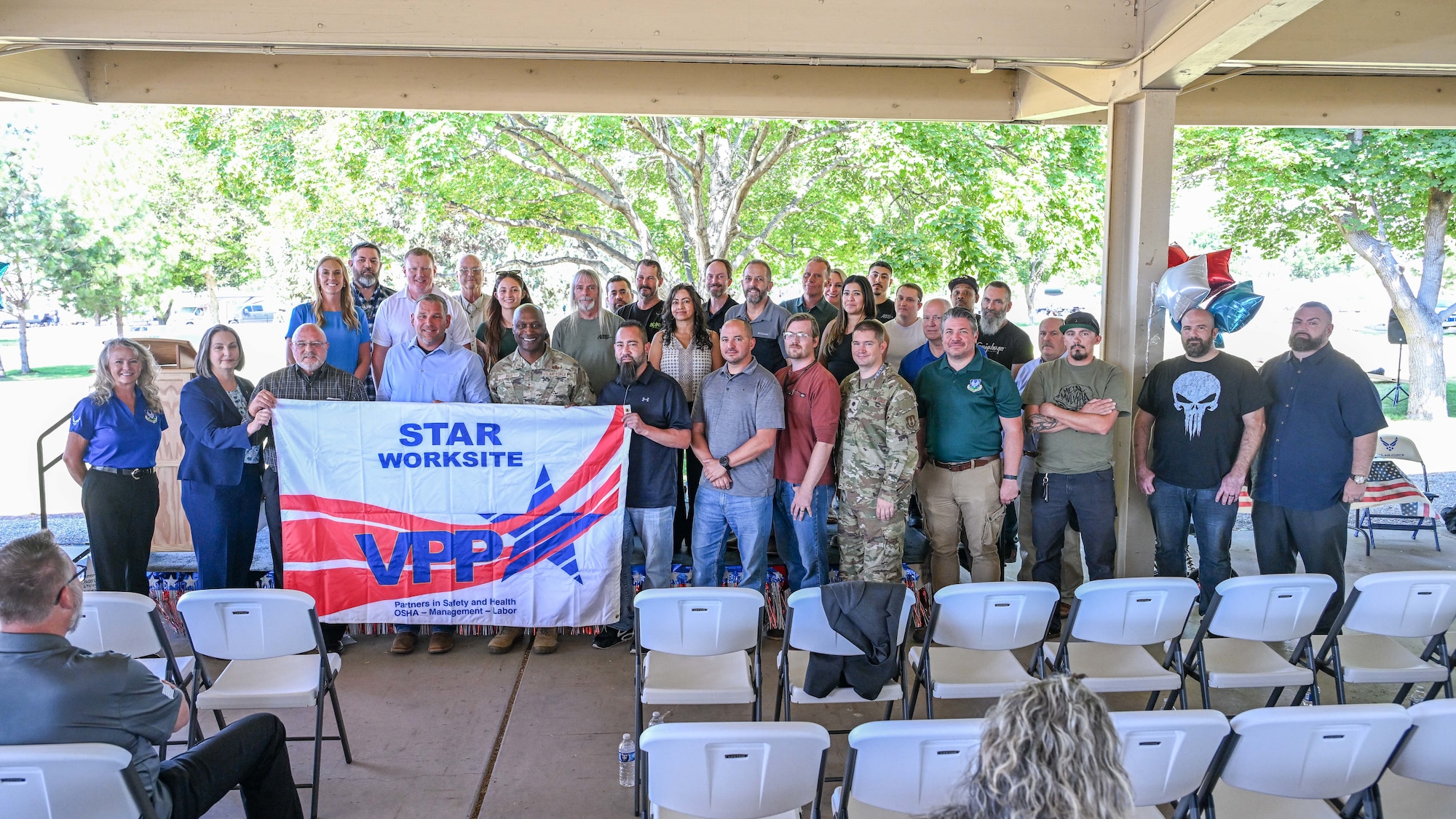 A mix of Ogden Air Logistics Complex leadership and 309th Maintenance Support Group employees pose together holding a VPP Star Site banner during an outdoor ceremony.