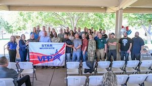A mix of Ogden Air Logistics Complex leadership and 309th Maintenance Support Group employees pose together holding a VPP Star Site banner during an outdoor ceremony.