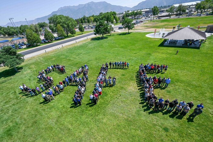 A large group of employees from the 309th Maintenance Support Group stands in a grassy field, arranged to spell the word “SAFE.”