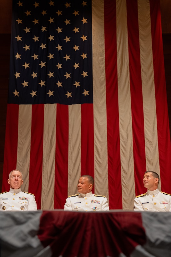 Acting Commandant of the Coast Guard Adm. Kevin Lunday (left to right), Rear Adm. Michael Johnston, and U.S. Coast Guard Academy (USCGA) Superintendent Rear Adm. Gregory Rothrock are seated onstage during a change of command ceremony inside Leamy Hall at USCGA, New London, Connecticut, July 16, 2025. Johnston was relieved by Rothrock who became the 44th superintendent of USCGA. (U.S. Coast Guard photo by Petty Officer Third Class Leo Avila.)