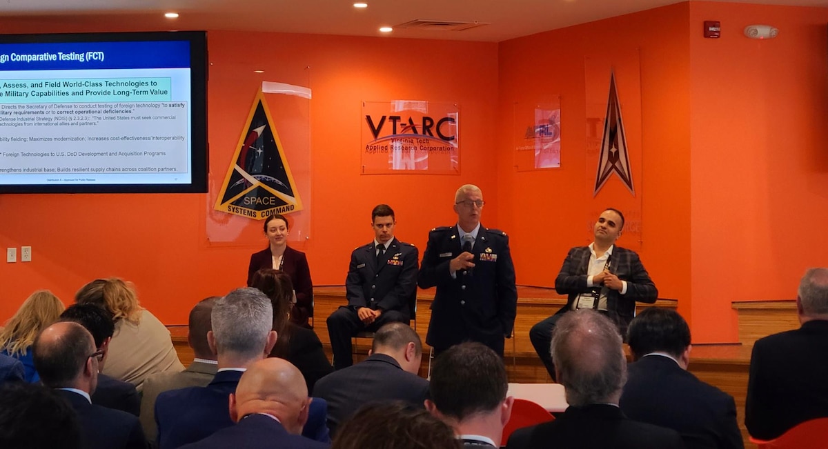 From left, Zoe Nelson, Front Door acquisition program manager; U.S. Air Force Maj. Brian Crouse, Headquarters U.S. Space Force, Global Partnerships Directorate; and U.S. Army Maj. Robert Perez-Alemany, technical program manager, space portfolio, Defense Innovation Unit & Space Development Agency, look on as U.S. Air Force Col. Jeffrey Naff, director of Foreign Comparative Testing, Office of the Under Secretary of Defense for Research and Engineering,  addresses a group of international vendors and government partners in Colorado Springs, Colo. April 9, 2025. U.S. Space Force Front Door hosted the inaugural event, welcoming over 100 international vendors representing 13 countries looking to partner with the Department of Defense and other governmental agencies within the space domain. (Courtesy Photo)